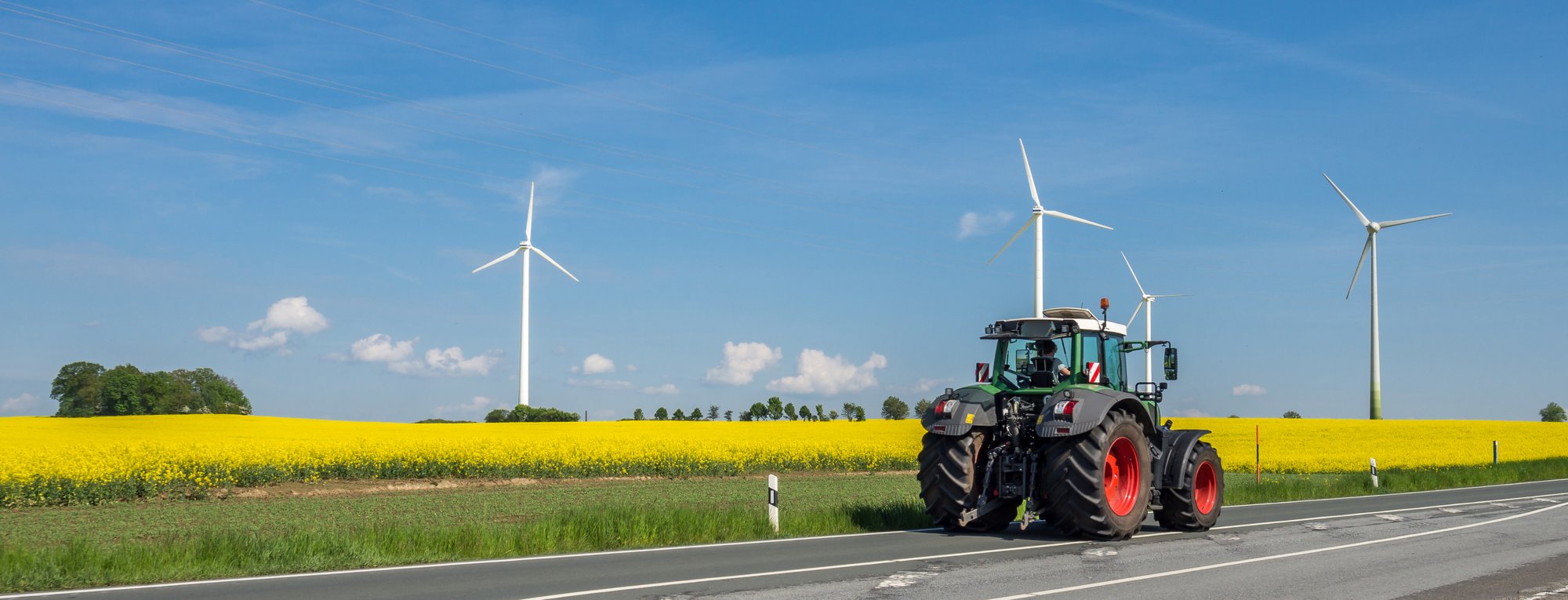 Landwirtschaftlicher Traktor neben einem Feld mit Windkraftanlagen im Hintergrund