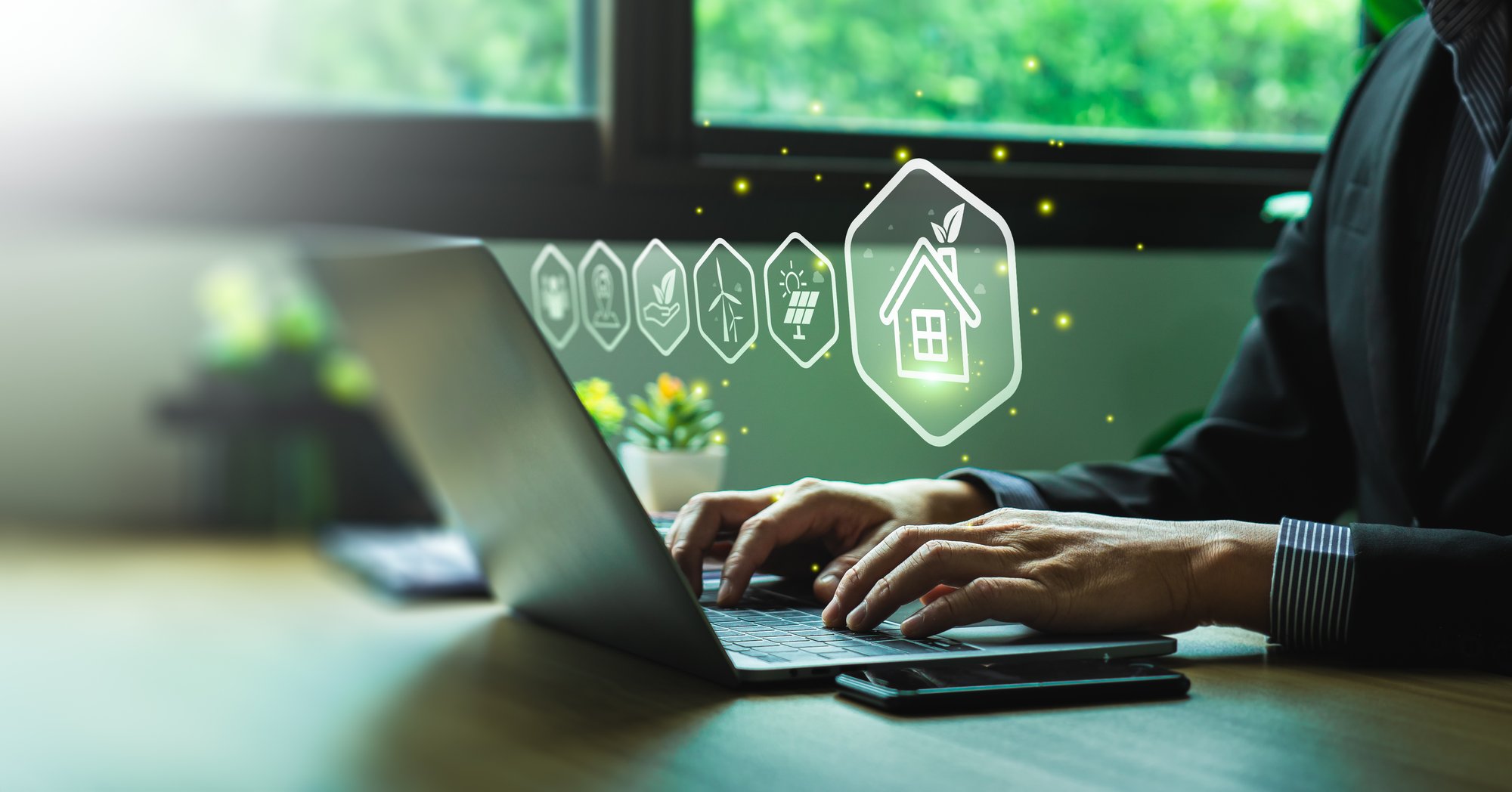 Person using a laptop with digital sustainability and energy management icons displayed above the keyboard.