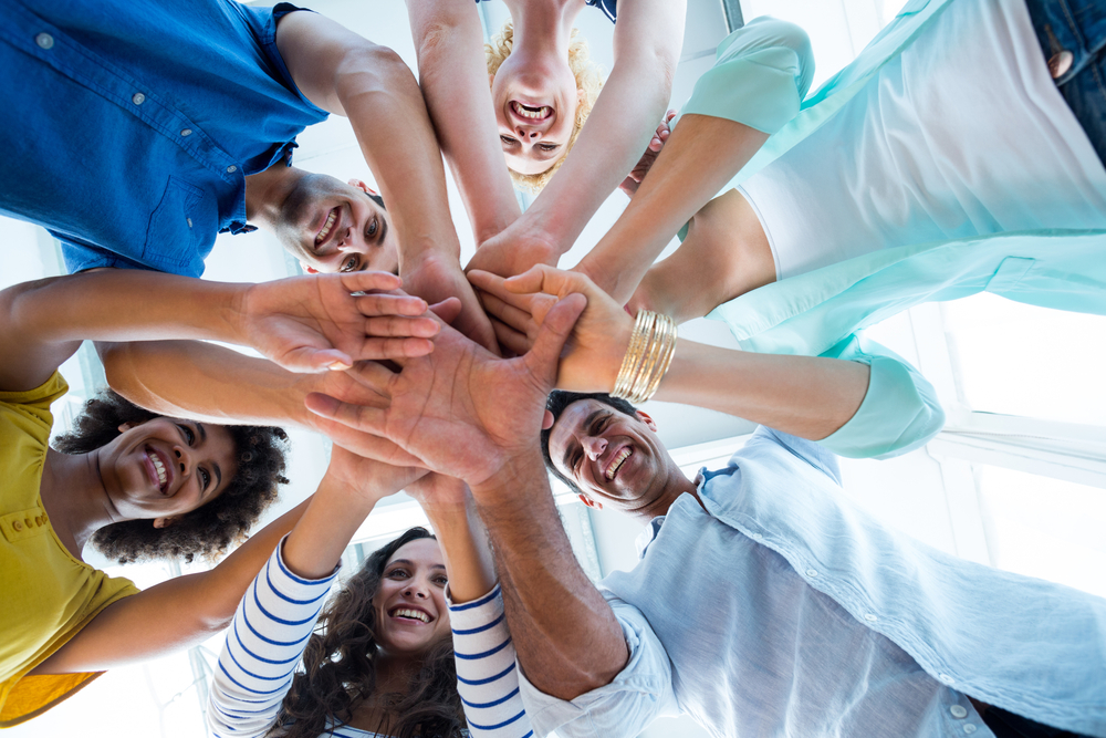 Team members stacking their hands together in a group huddle, viewed from below.