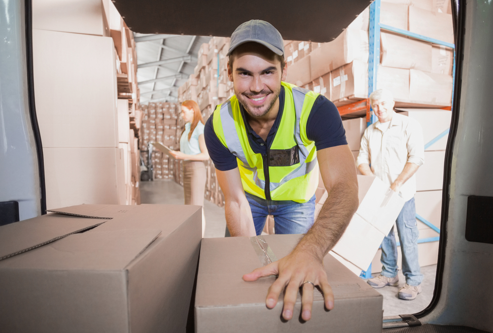 Warehouse worker loading cardboard boxes into a delivery vehicle inside a distribution center.