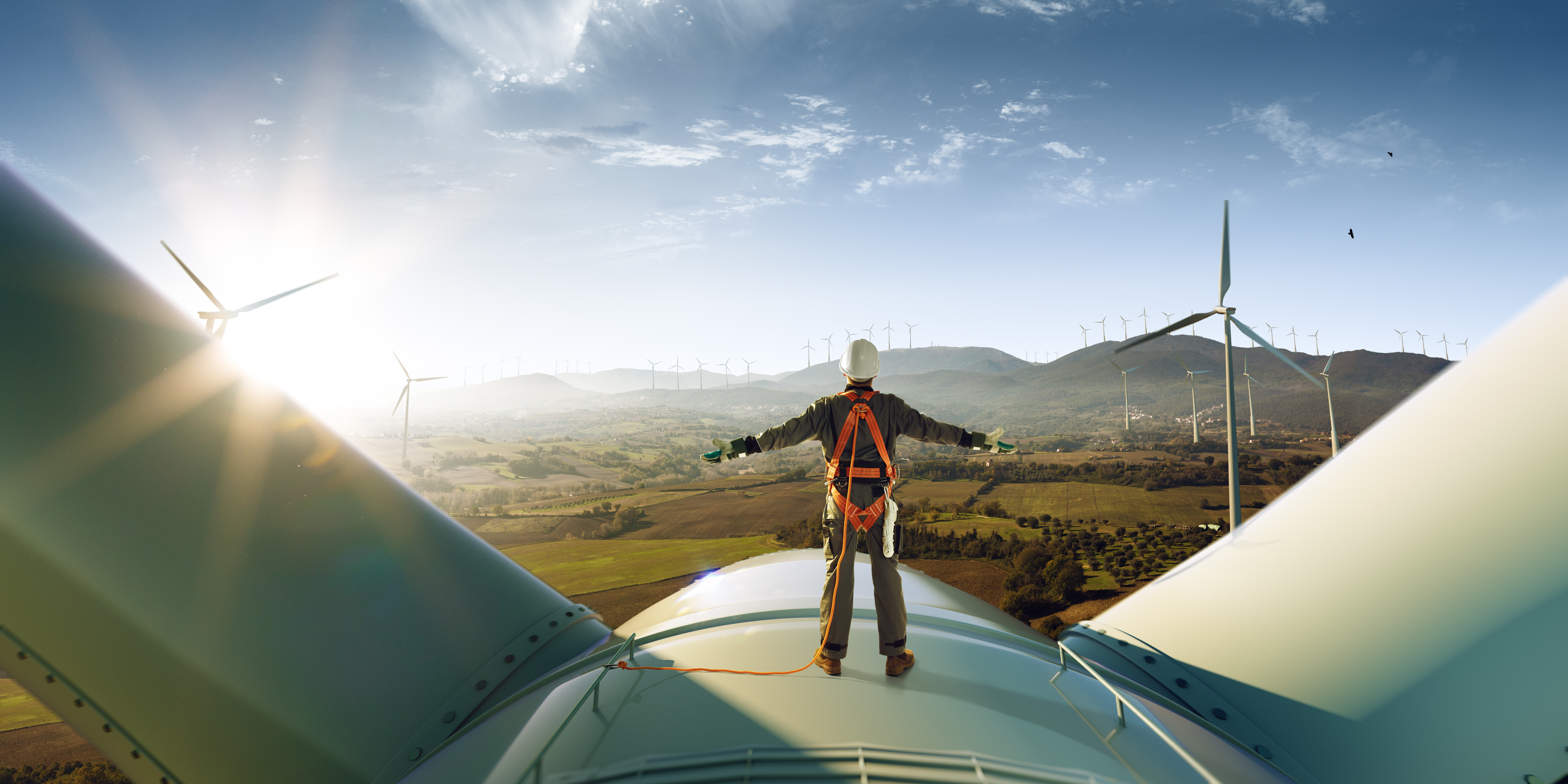 Technician standing on top of a wind turbine overlooking a renewable energy landscape with multiple wind turbines