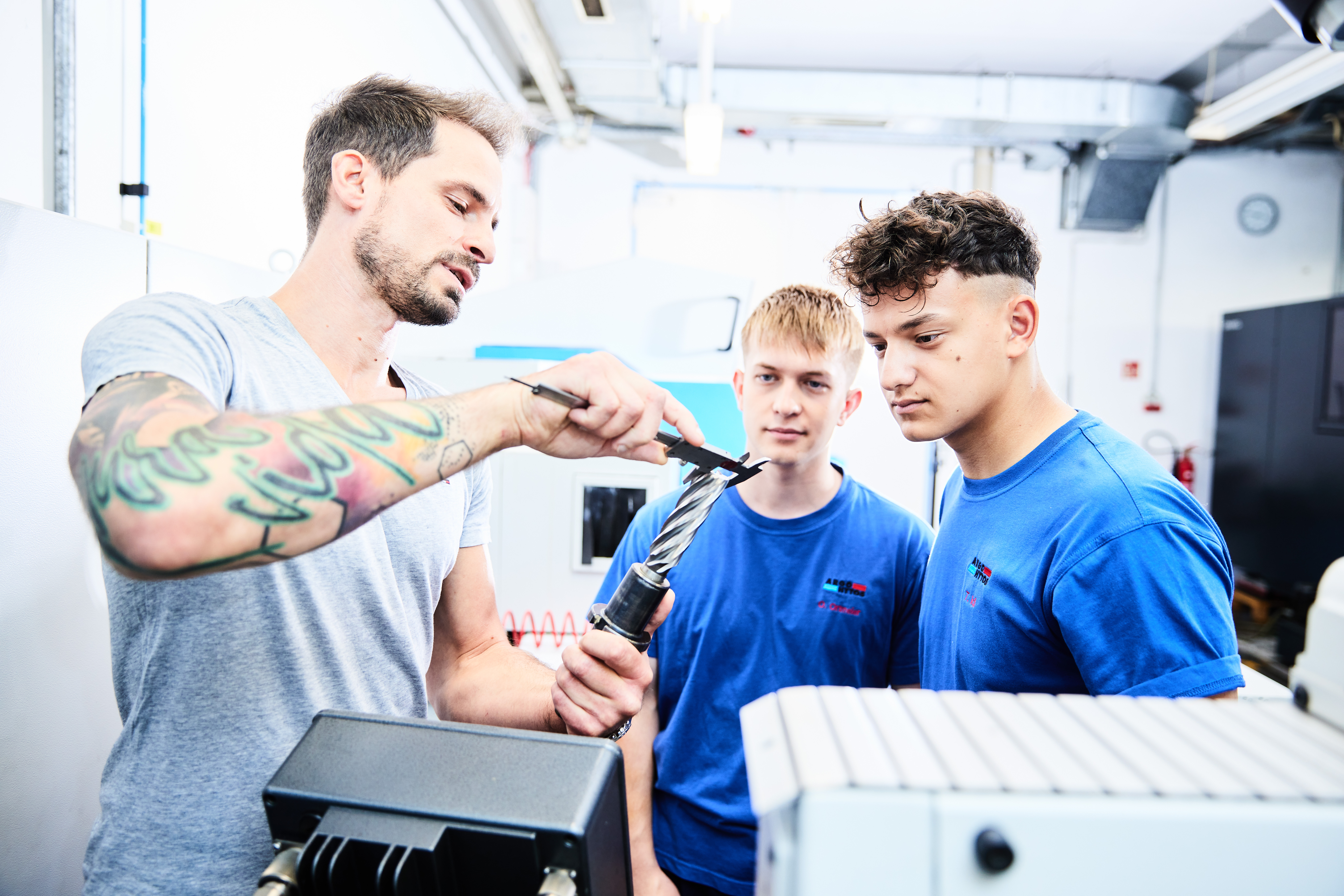 Ausbildende Person erklärt eine technische Komponente an Teilnehmende in einer Werkstatt oder Schulungsumgebung.