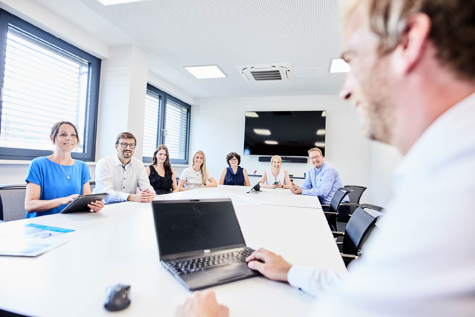 Mitarbeitende sitzen während einer Besprechung an einem Konferenztisch in einem modernen Besprechungsraum.