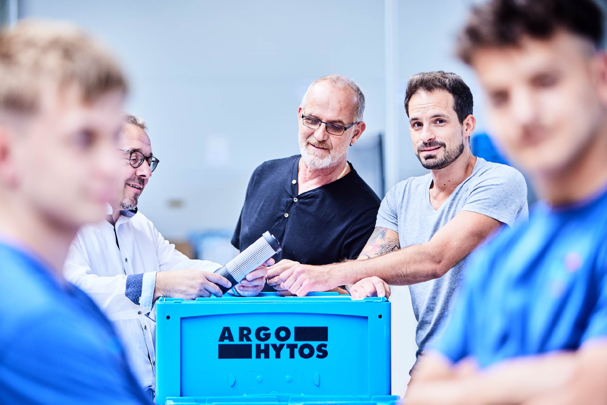 Mitarbeitende stehen für eine Besprechung um einen ARGO-HYTOS-Behälter in einer Produktionsumgebung. Mitarbeitende stehen für eine Besprechung um einen ARGO-HYTOS-Behälter in einer Produktionsumgebung.