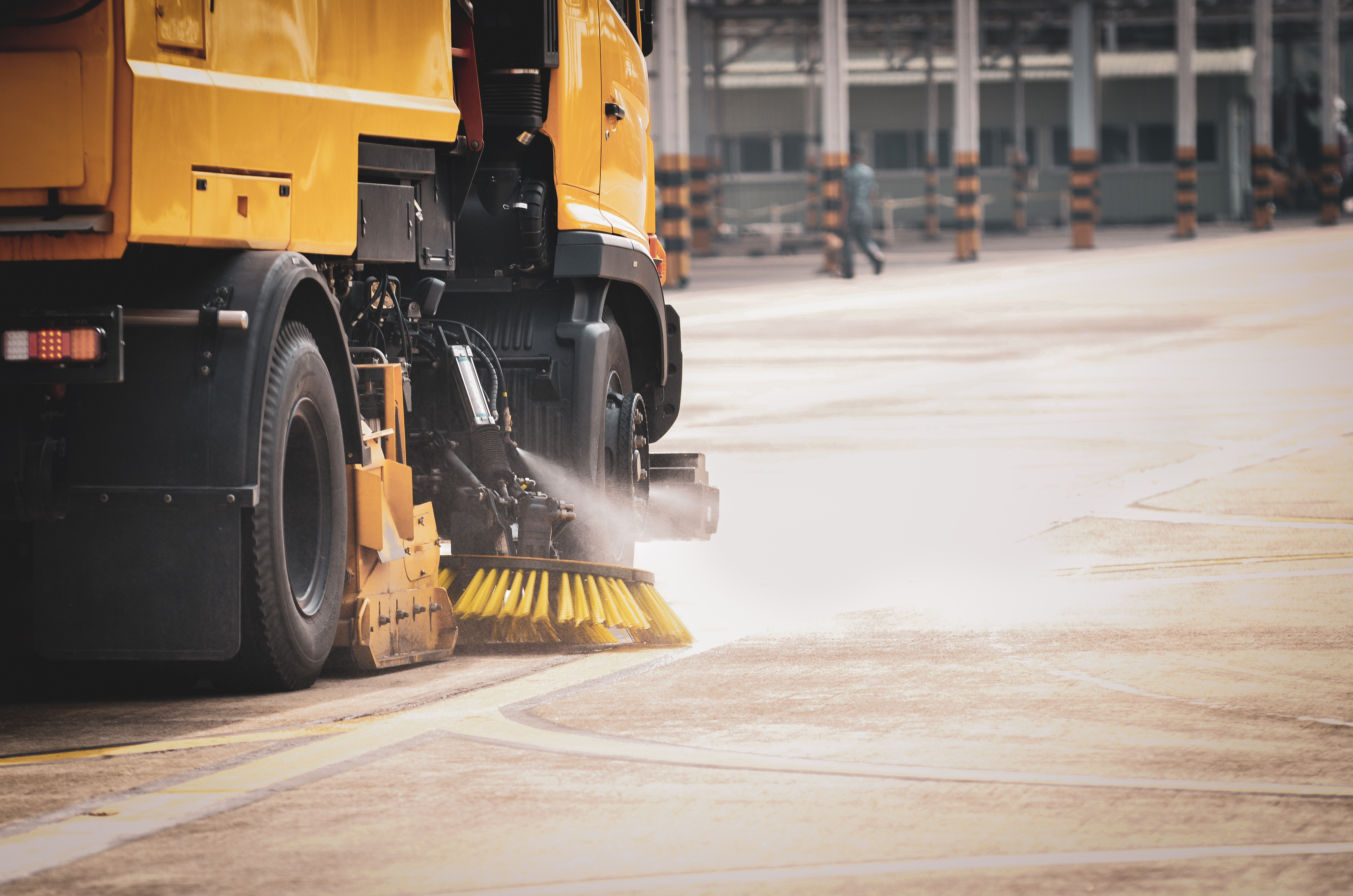 Street sweeper cleaning an industrial roadway with rotating brushes and water spray system