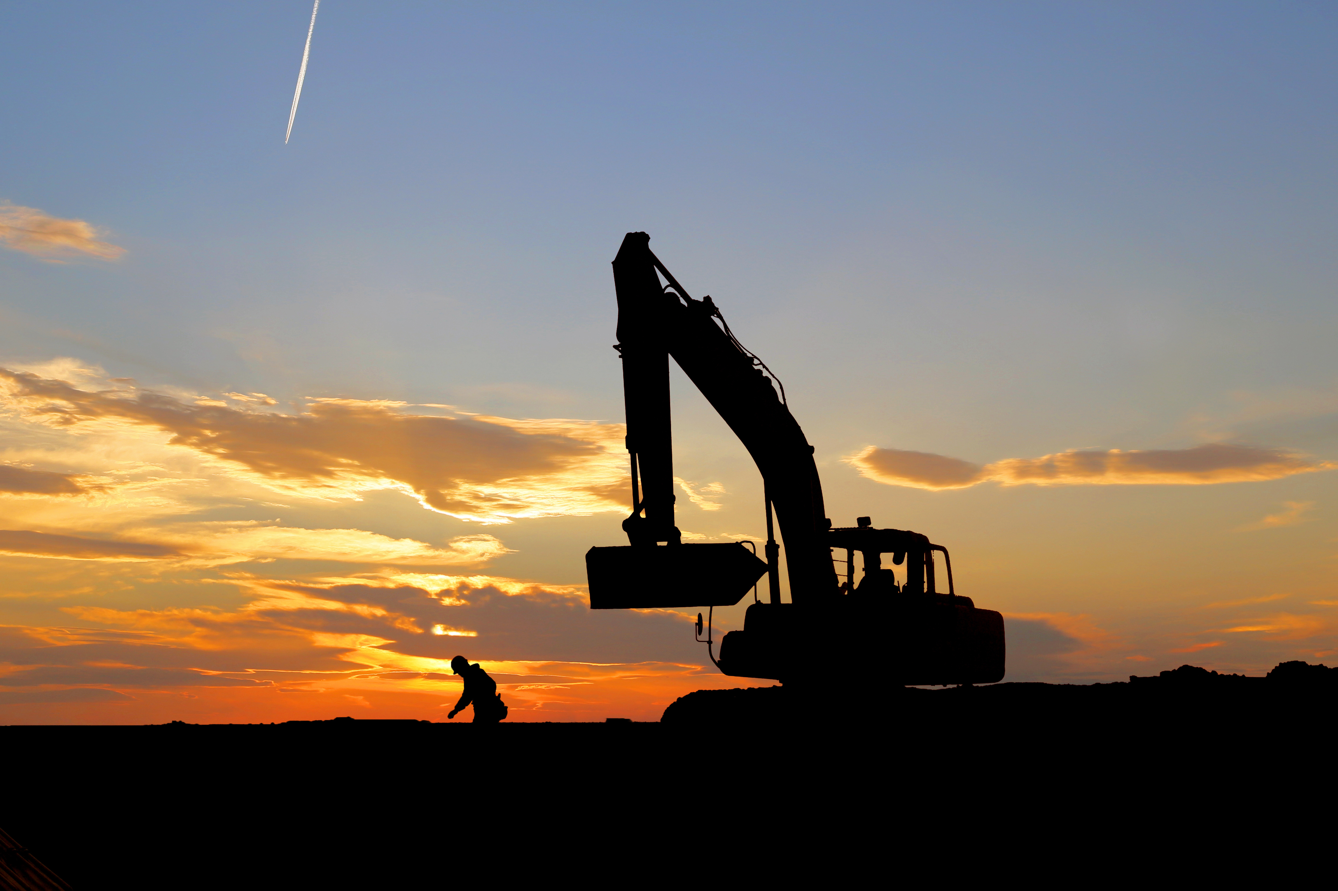 Hydraulic excavator at a construction site silhouetted against a sunset sky