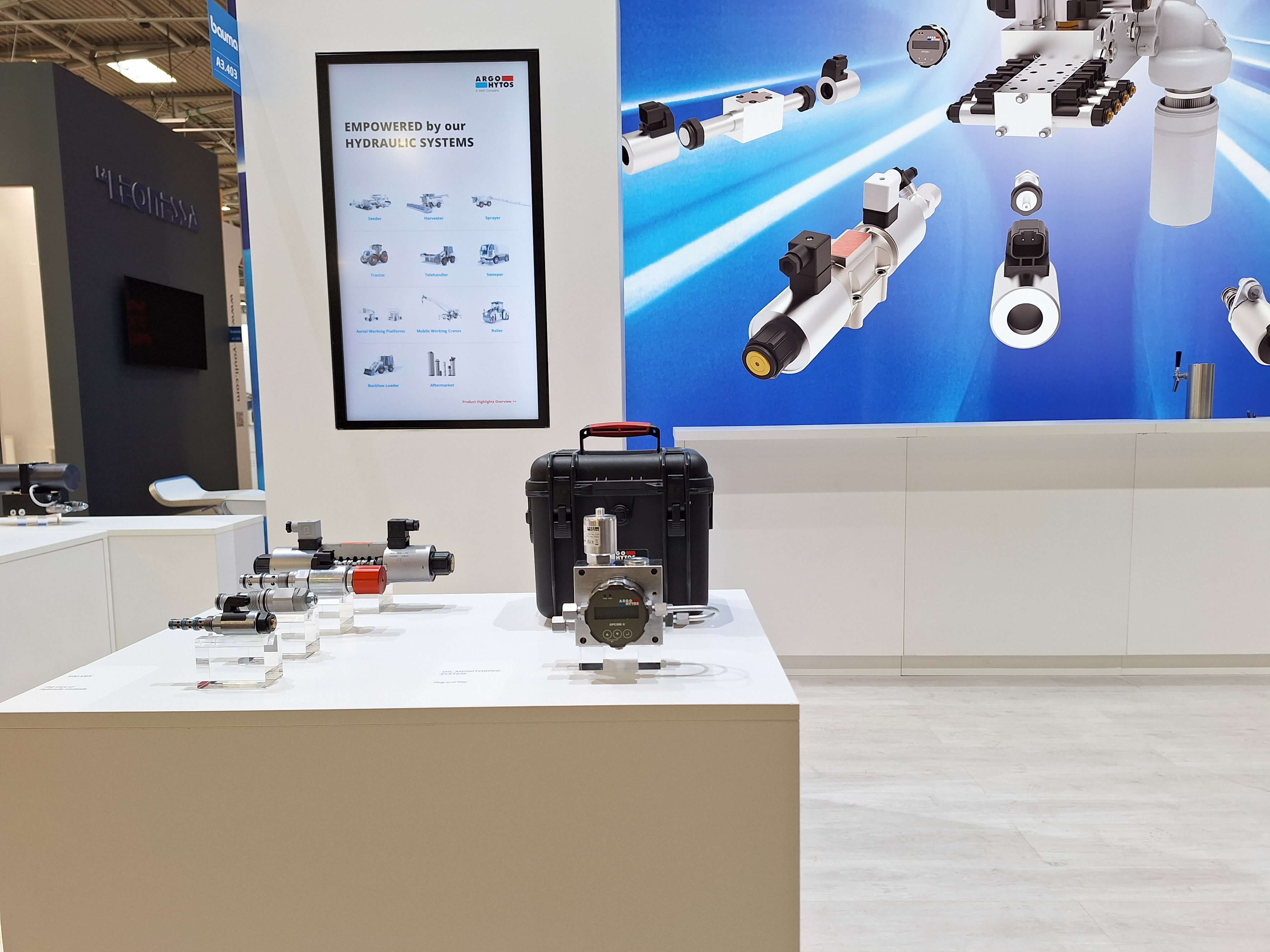 Messestand mit ausgestellten Hydraulikkomponenten auf Präsentationstischen und großflächiger Produktgrafik im Hintergrund.