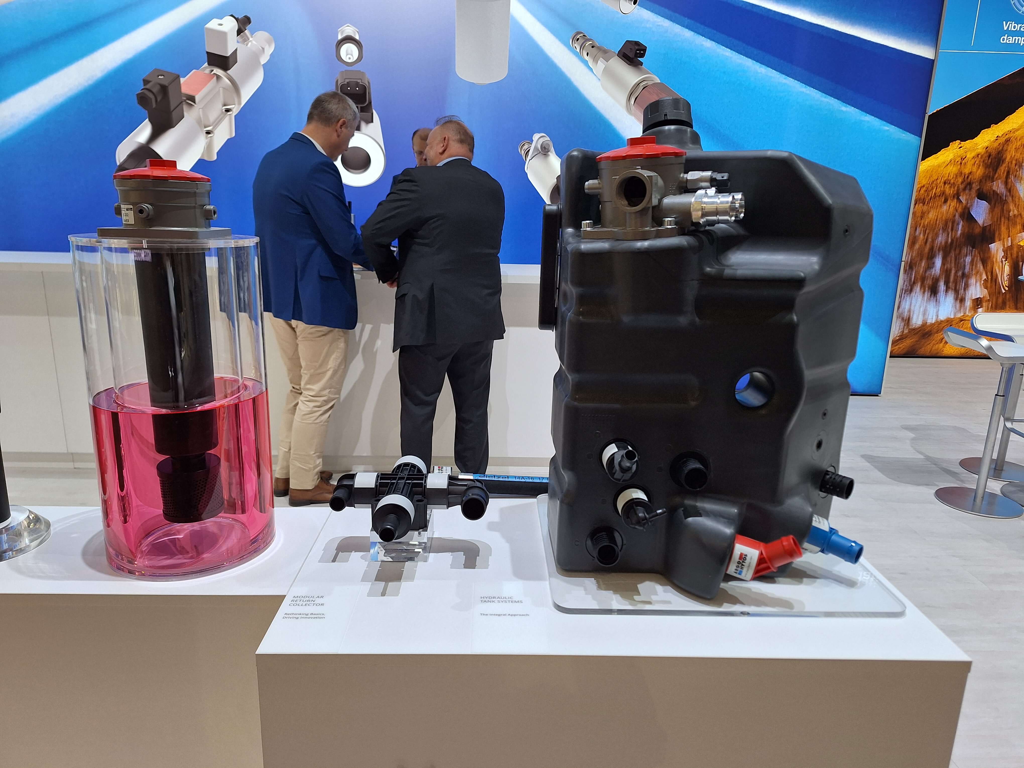 Tanklösung und Filterkomponenten auf einem Messestand, mit Besuchern und Produktgrafiken im Hintergrund.