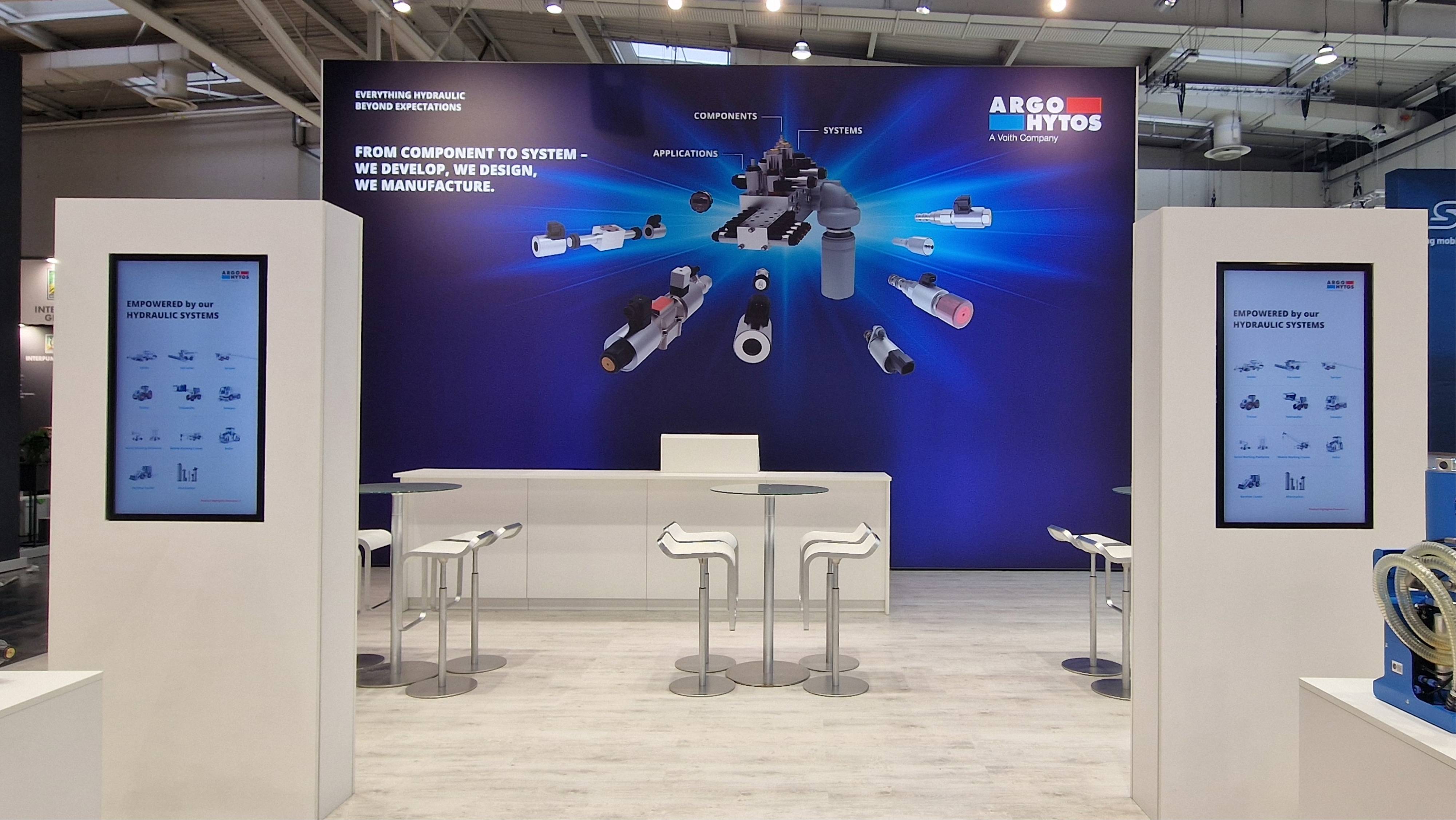 ARGO-HYTOS Messestand mit digitalen Informationsdisplays und großformatigen Grafiken von Hydraulikkomponenten.  Geben Sie Ihr Feedback zu BizChat ab.