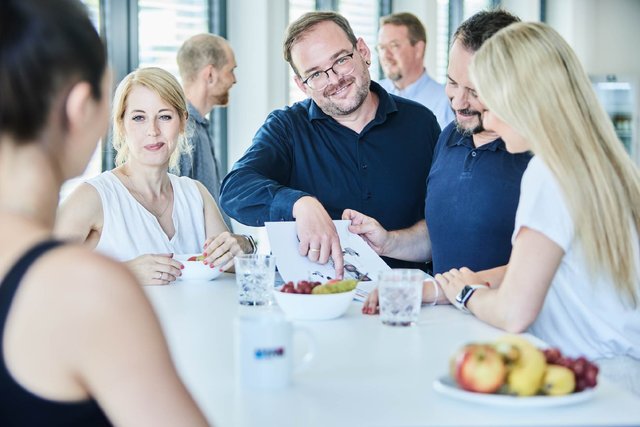 Personen an einem Besprechungstisch während eines Teammeetings in einer modernen Büroumgebung