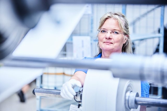 Employee operating industrial machinery with a large material roll in a production environment. Employee operating industrial machinery with a large material roll in a production environment.