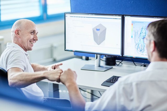 Zwei Mitarbeitende besprechen ein 3D-CAD-Modell an einem Arbeitsplatz mit zwei Bildschirmen.