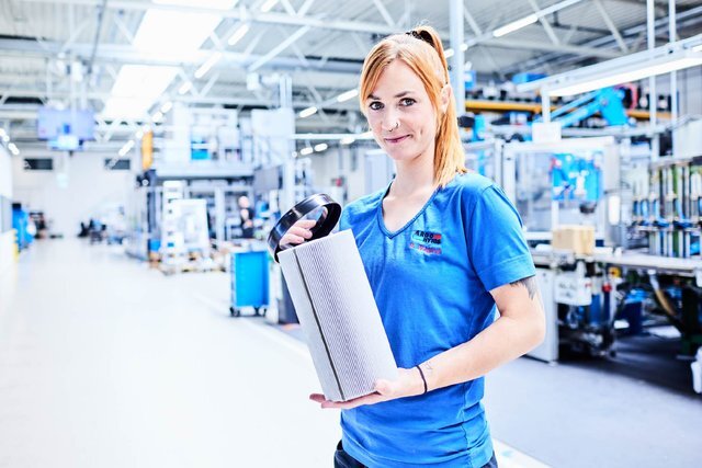 Mitarbeitende hält ein zylindrisches Industrie-Filterelement in einer Produktionshalle.